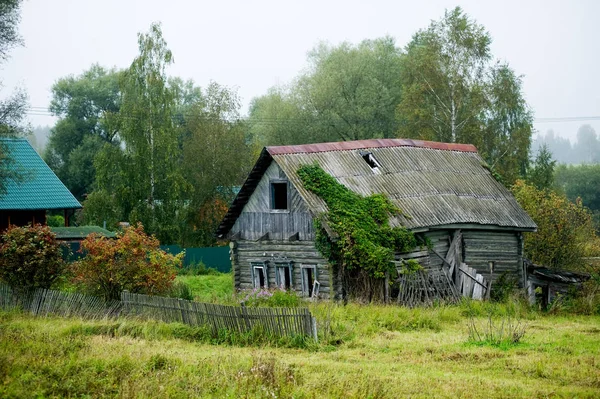 Vecchia casa traballante in un villaggio lontano. Trama coperta d'erba — Foto Stock