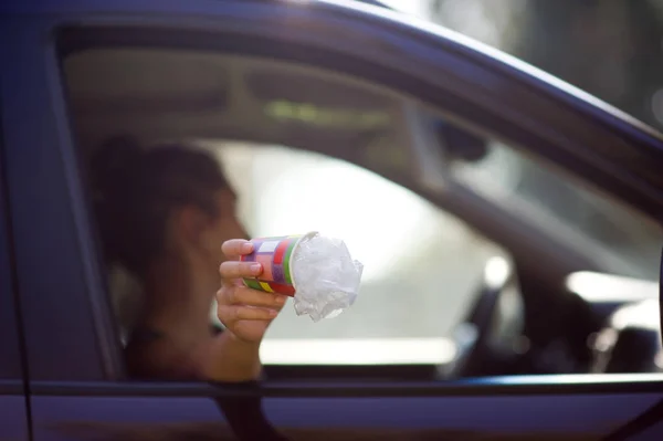 Lány tartja szemetet kívül autó ablakon. Egy nő arra készül, hogy dobja a hulladékot egy autóból. Környezetszennyezés, szelektív fókusz — Stock Fotó