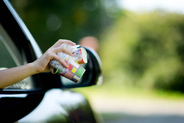 Girl holds trash outside the car window. A woman is about to throw waste out of a car. Environmental pollution, selective focus