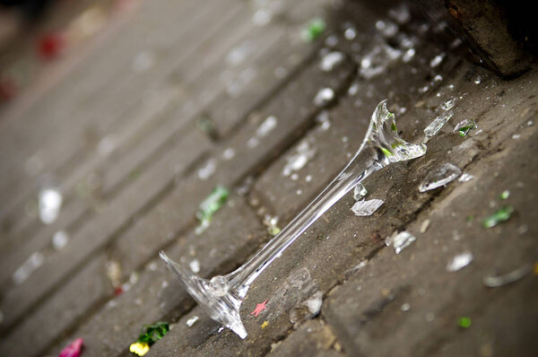 Разбитый бокал шампанского лежит на тротуаре.
