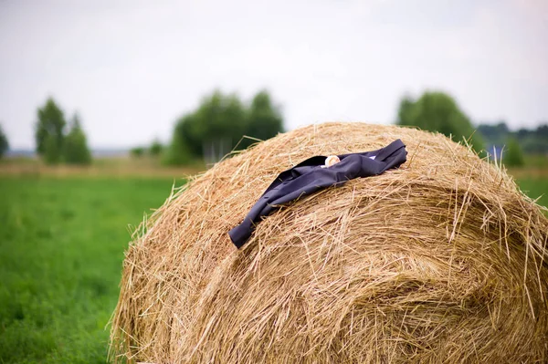 A man s jacket with a boutonniere lies on a haystack on a cloudy summer day in the village. — Stock Photo, Image