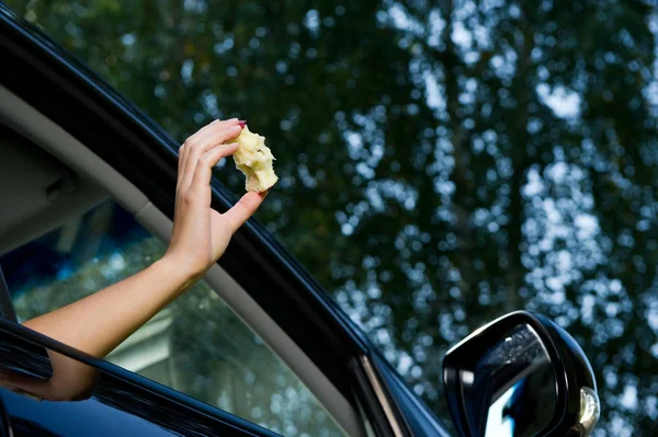 La femme se tient dehors et est sur le point de jeter un noyau de pomme par la fenêtre ouverte de la voiture. Vue du bas, sur fond d'arbres flous et de ciel. Gros plan — Photo