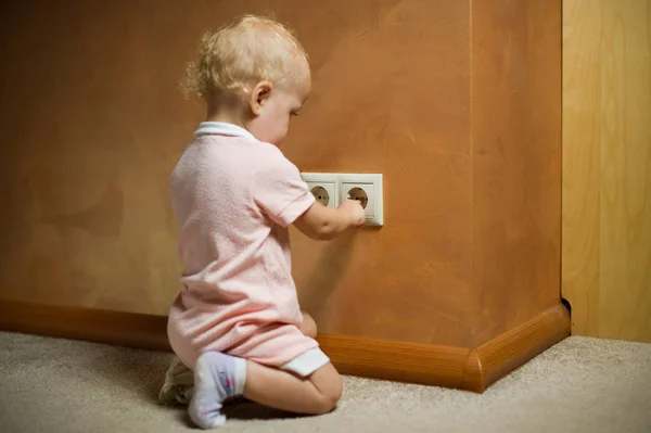 Petite fille joue avec une prise électrique. Un enfant enfonce ses doigts dans une prise vivante — Photo