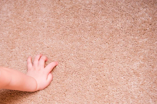 Маленькая детская рука лежит на ковре на полу — стоковое фото