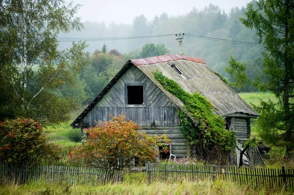 Régi elhagyott rozoga régi fából készült ház nélküli ablakok egy részlegesen hiányzó kerítés. Fűvel borított telek — Stock Fotó