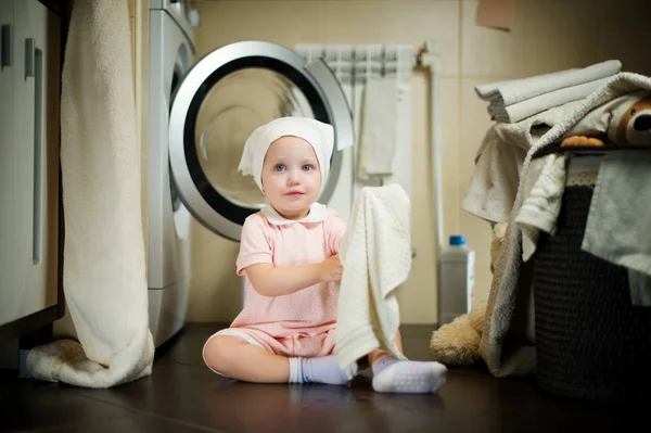 Mädchen sitzt mit Handtuch in der Hand neben der Waschmaschine im Badezimmer — Stockfoto