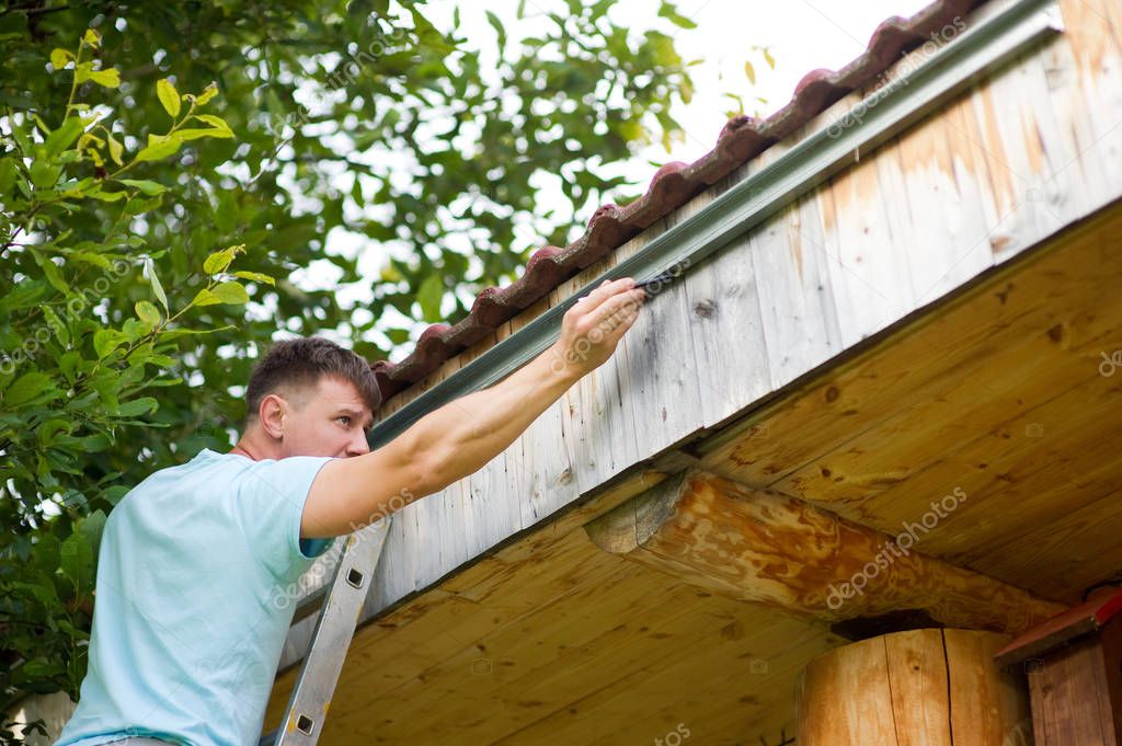 the man is concentrated, he puts the markup to install the gutter on a wooden house