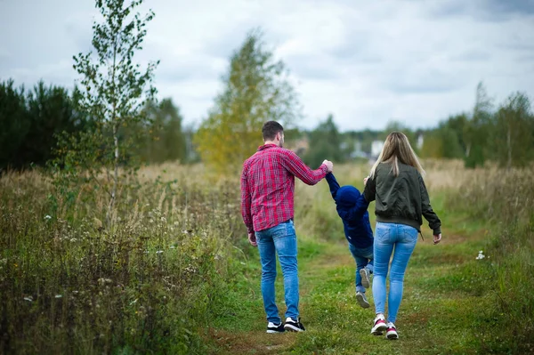 Young parents playfully walk with their little son along a country road, rear view