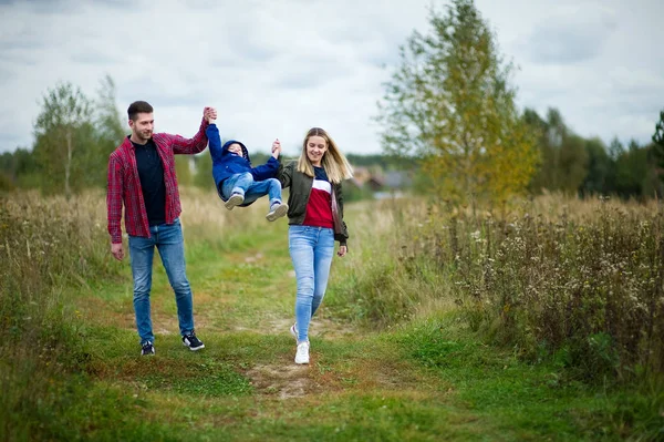 Pais em roupas casuais caminham com um pequeno filho em uma estrada de campo — Fotografia de Stock