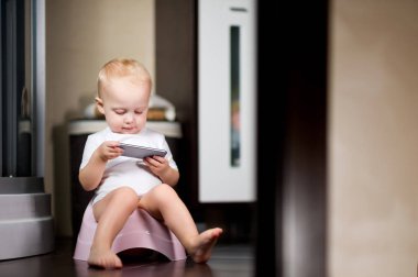 küçük kız elinde bir akıllı telefon tutan banyoda bir tencere üzerinde oturan