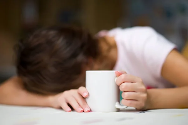 Menina adormeceu na mesa segurando uma caneca branca de café — Fotografia de Stock