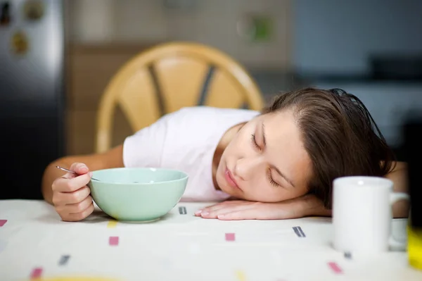 Menina adormeceu na mesa no café da manhã, segurando uma colher em um prato com bolas de chocolate e leite — Fotografia de Stock