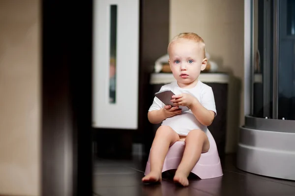 Enfant tient un smartphone dans ses mains assis sur un pot dans la salle de bain — Photo