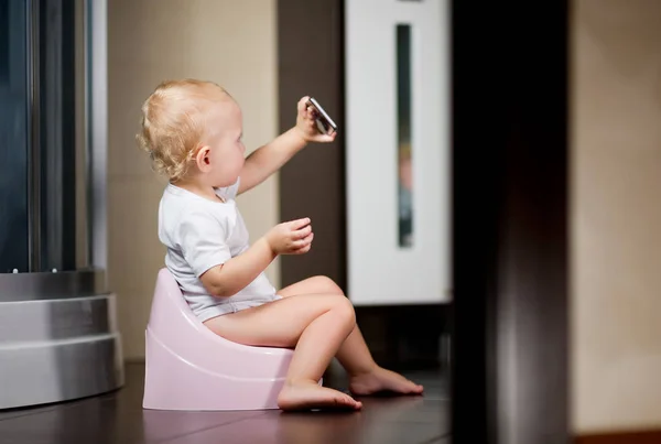 Kleines Mädchen sitzt auf einem Topf im Badezimmer und macht ein Selfie mit dem Smartphone — Stockfoto