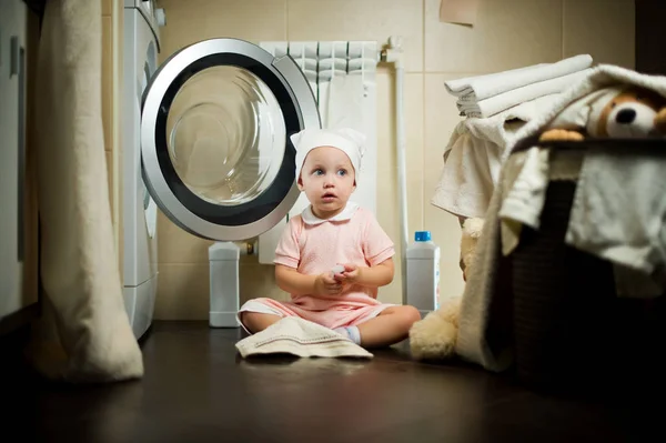 Mädchen sitzt neben der Waschmaschine auf dem Fußboden im Badezimmer. — Stockfoto