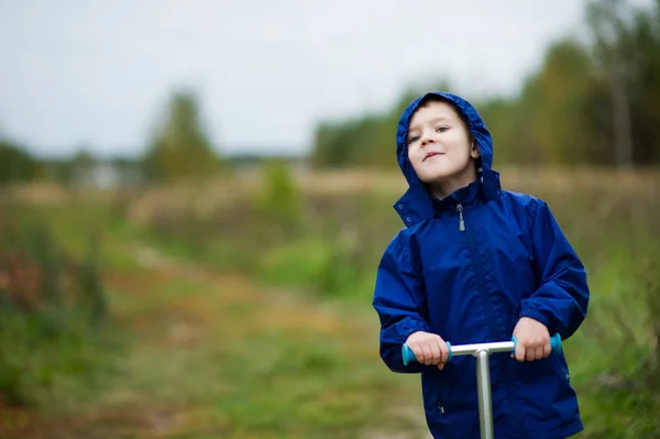 Köyde bir scooter üzerinde mavi ceket ve bir başlık bir çocuk mesafe içine bakar — Stok fotoğraf