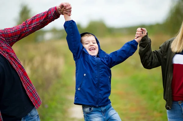 Föräldrar höjer sin skrattande son i en blå jacka i luften av händerna. I ramen, bara en pojke och händerna på föräldrarna — Stockfoto
