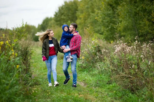 Uma jovem família de três em roupas casuais caminha ao longo de uma estrada rural na aldeia — Fotografia de Stock