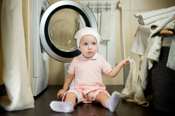 Ein kleines Kind in der Nähe der Waschmaschine schaut weg und hält ein Handtuch in der Hand — Stockfoto