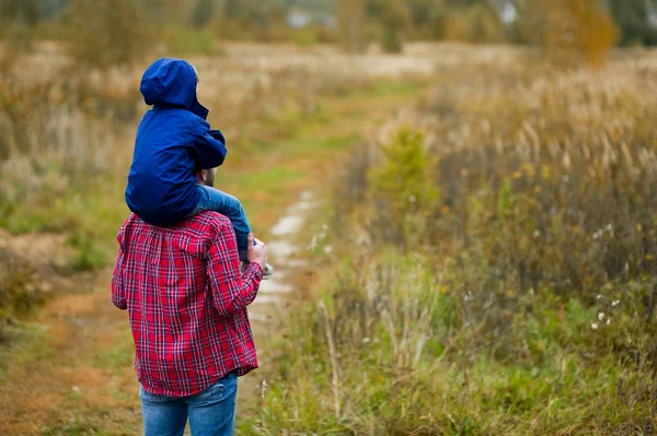 Sonen sitter på sin fars axlar. Far och son i byn. Tonas. Kopiera utrymme — Stockfoto