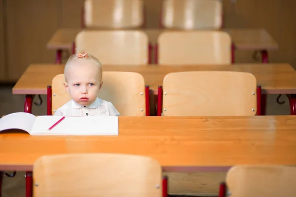 Pequeña niña preescolar se sienta en su escritorio y se ve muy molesto —  Fotos de Stock