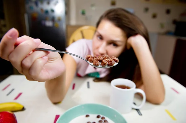 Het meisje kijkt helaas naar de lepel met chocoladevlokken die ze voor zichzelf vasthoudt. groothoek, selectieve scherpstelling — Stockfoto