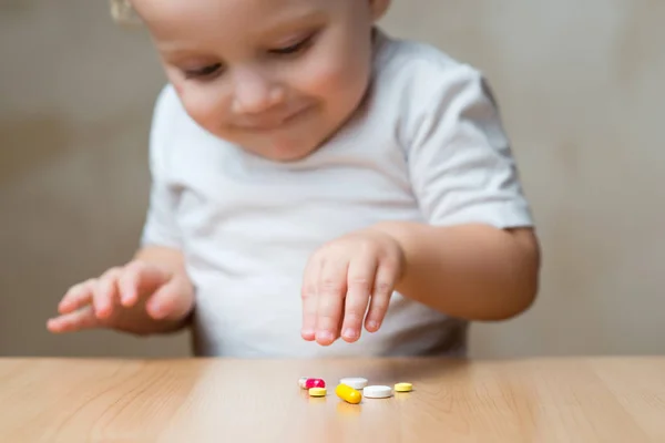 Un niño pequeño está a punto de tomar píldoras dejadas por adultos —  Fotos de Stock