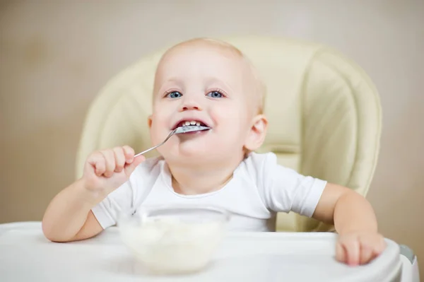 Улыбающийся ребенок в кресле для кормления держит ложку во рту и улыбается — стоковое фото