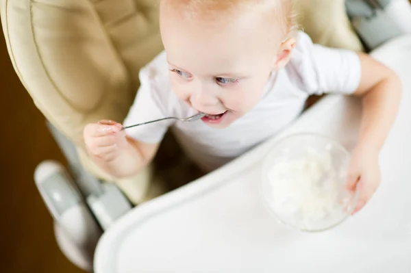 Menina em um assento de bebê para alimentação come mingau de cereal, sorrindo alegremente, vista superior — Fotografia de Stock
