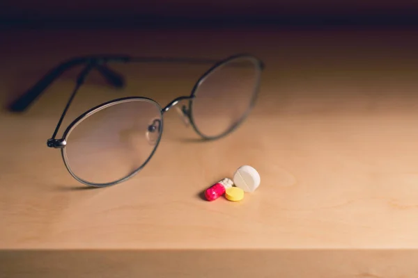 Copos para a visão e uma porção de comprimidos encontra-se em uma prateleira, close-up, tonificado — Fotografia de Stock