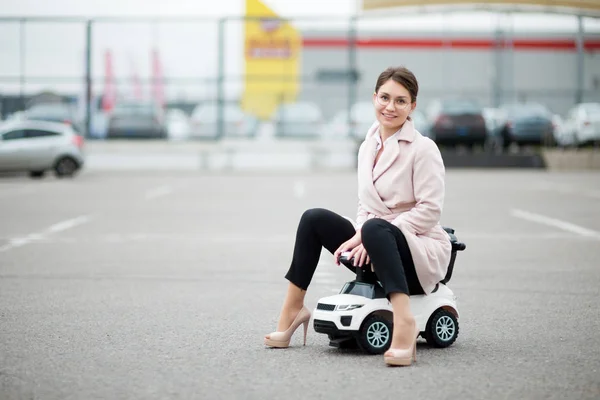 Flicka i rock sitter på en plastbil för ett barn — Stockfoto