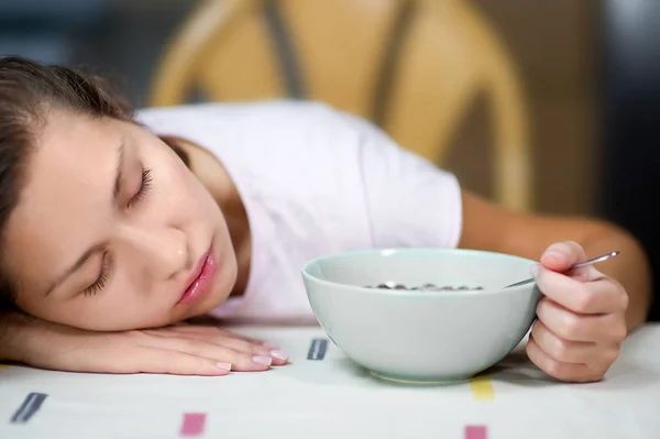 Mulher adormeceu na mesa no café da manhã, segurando uma colher em um prato com bolas de chocolate e leite — Fotografia de Stock