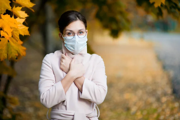 Une fille dans un masque médical ferme son col de manteau plus étroitement un jour d'automne — Photo