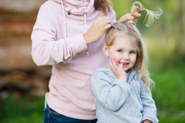 Retrato de una niña sonriente cuya madre teje una trenza en una noche de verano — Foto de Stock