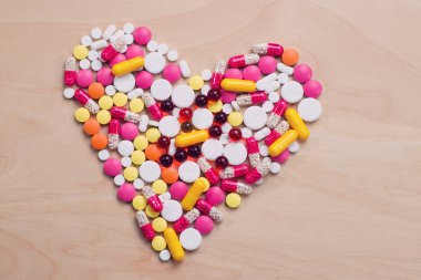 Tahta bir masanın üzerine kalp şeklinde bir avuç dolusu farklı hap bırakılmış.
