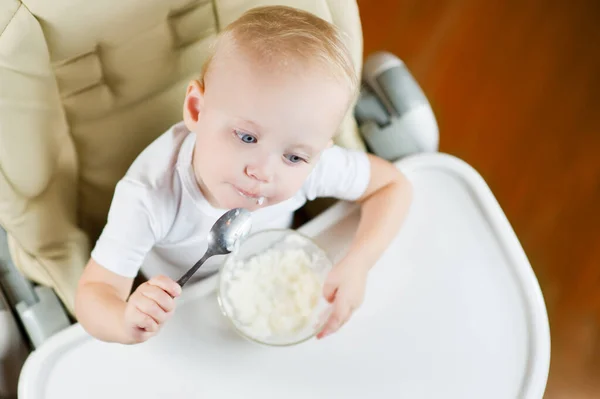 Une petite fille mange du porridge avec une cuillère et pense à quelque chose . — Photo