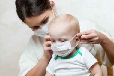 Anne küçük kızına tıbbi bir maske takıyor.
