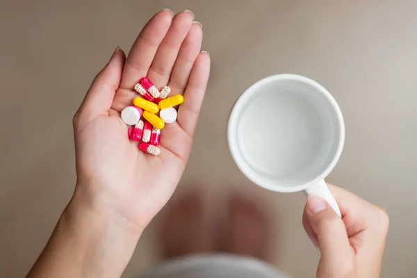 a handful of different pills and water in the hands of a young woman