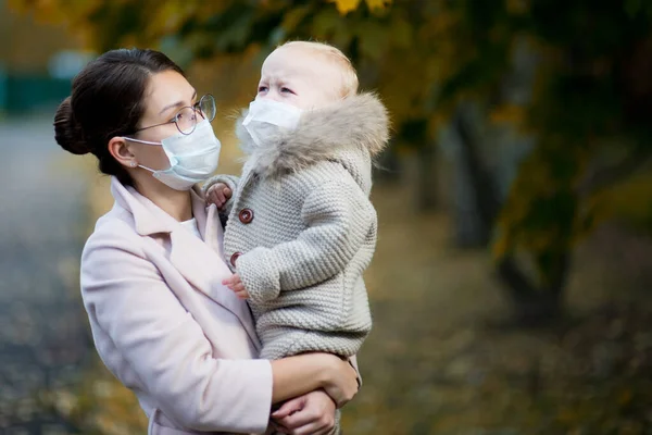 Tıbbi maskeli kadın kollarında ağlayan bir bebek tutuyor. — Stok fotoğraf