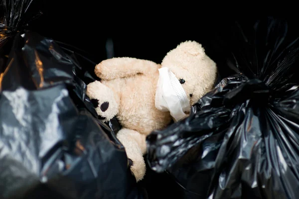 Un oso de peluche en una máscara médica se encuentra en el maletero de un coche en bolsas de basura — Foto de Stock