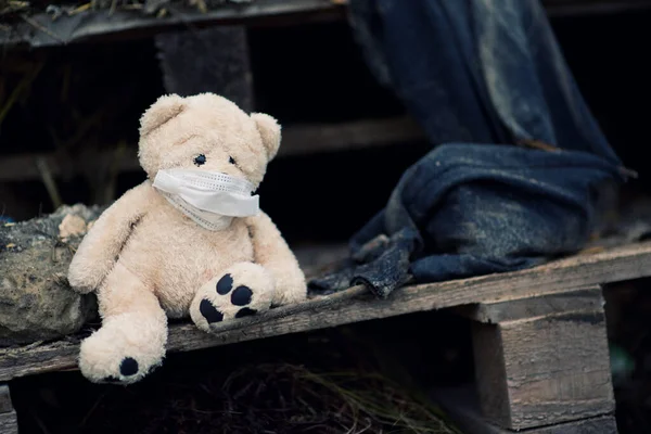 Um pequeno urso de pelúcia em uma máscara médica senta-se em uma palete em um aterro sanitário — Fotografia de Stock