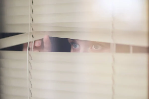 woman looking forward through the window blinds