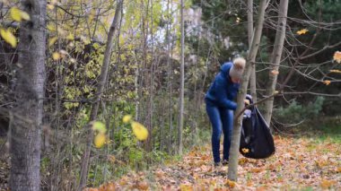 Genç kız gönüllü olarak bir torba içinde çöp topluyor, ormanı temizliyor.