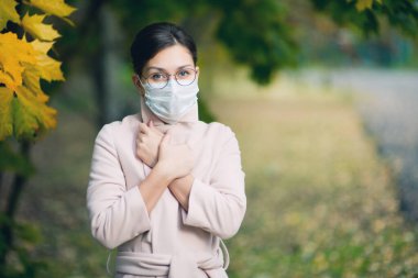 Tıbbi maske, ceket ve gözlüklü bir kadın ellerini göğsüne bastırıyor..