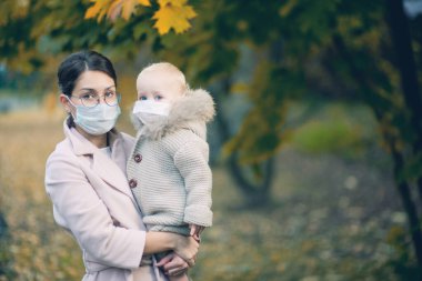 Anne ve küçük kızı sonbahar ormanında tıbbi maske takıyor.