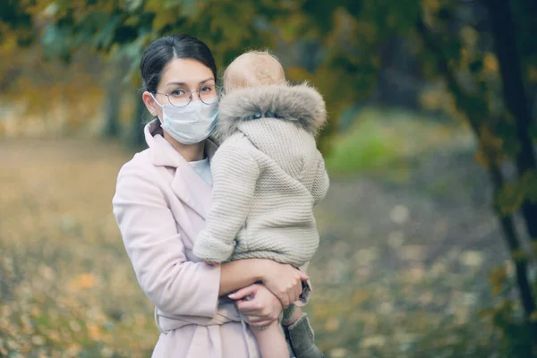 Une femme dans un masque facial tient dans ses bras un petit enfant qui s'est détourné — Photo