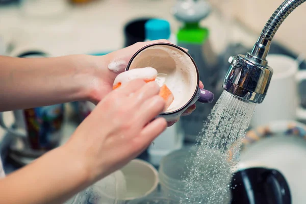 Chica enjabona una taza en el fondo de platos sucios —  Fotos de Stock