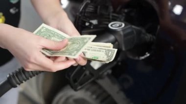 Eller, mazot dolduran arabanın arka planına kıyasla buruşmuş dolarları sayar.