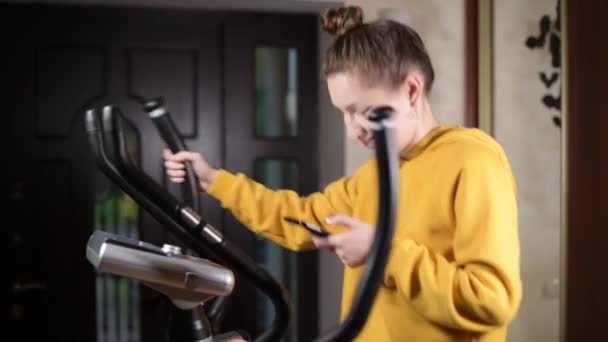 Uma Garota Uma Camisola Amarela Treina Elipsoide Olha Para Telefone — Vídeo de Stock