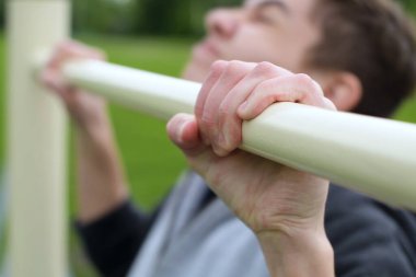 Genç çubuğu kapar ve kendini yukarı çekmeye başlar. Temiz havada gençlik eğitimi. Seçici odak, kapat